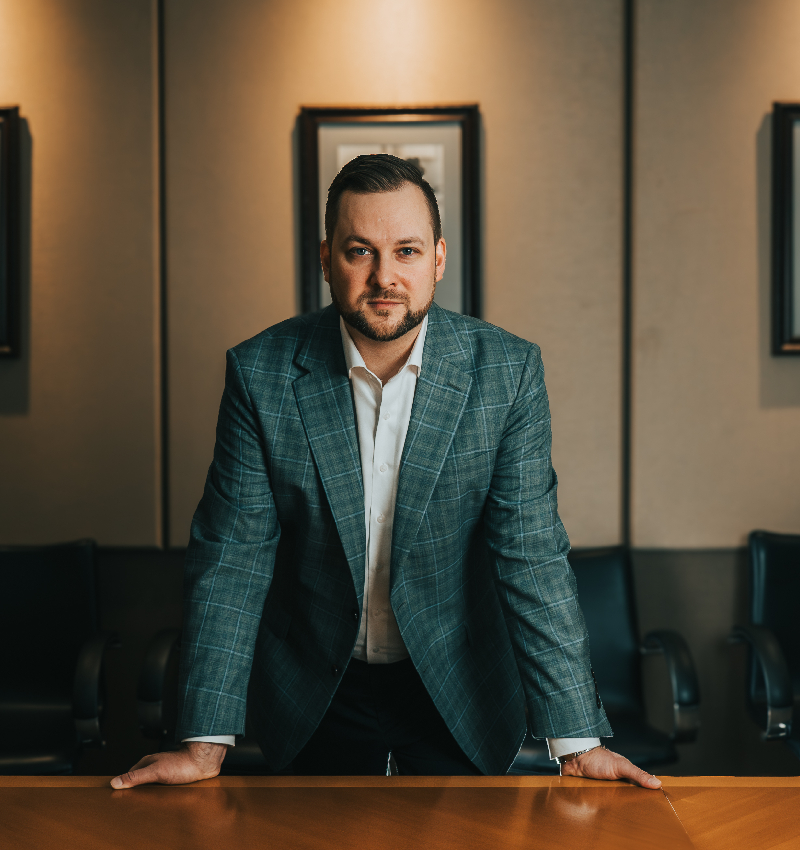 JJ in suit stands confidently in front of a table, exuding professionalism and poise in a formal setting.