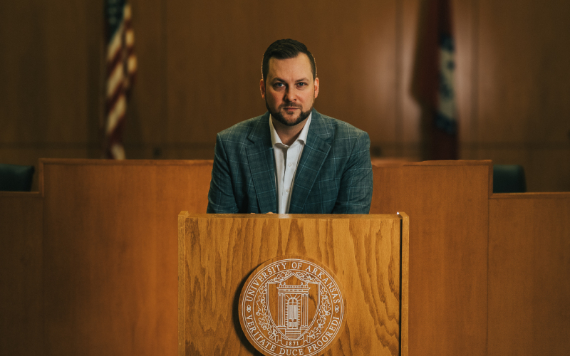 JJ stands behind a podium, poised to deliver a speech, exuding professionalism and authority.