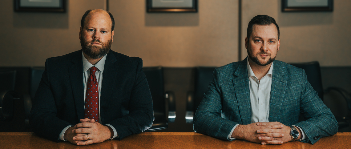 JJ and Harrison, both in suits, are sitting at a table, looking professional