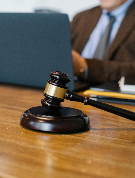 Photograph of a gavel on a wooden desk, lawyer and laptop in the background, lawyer studying the case of legal rights violations.